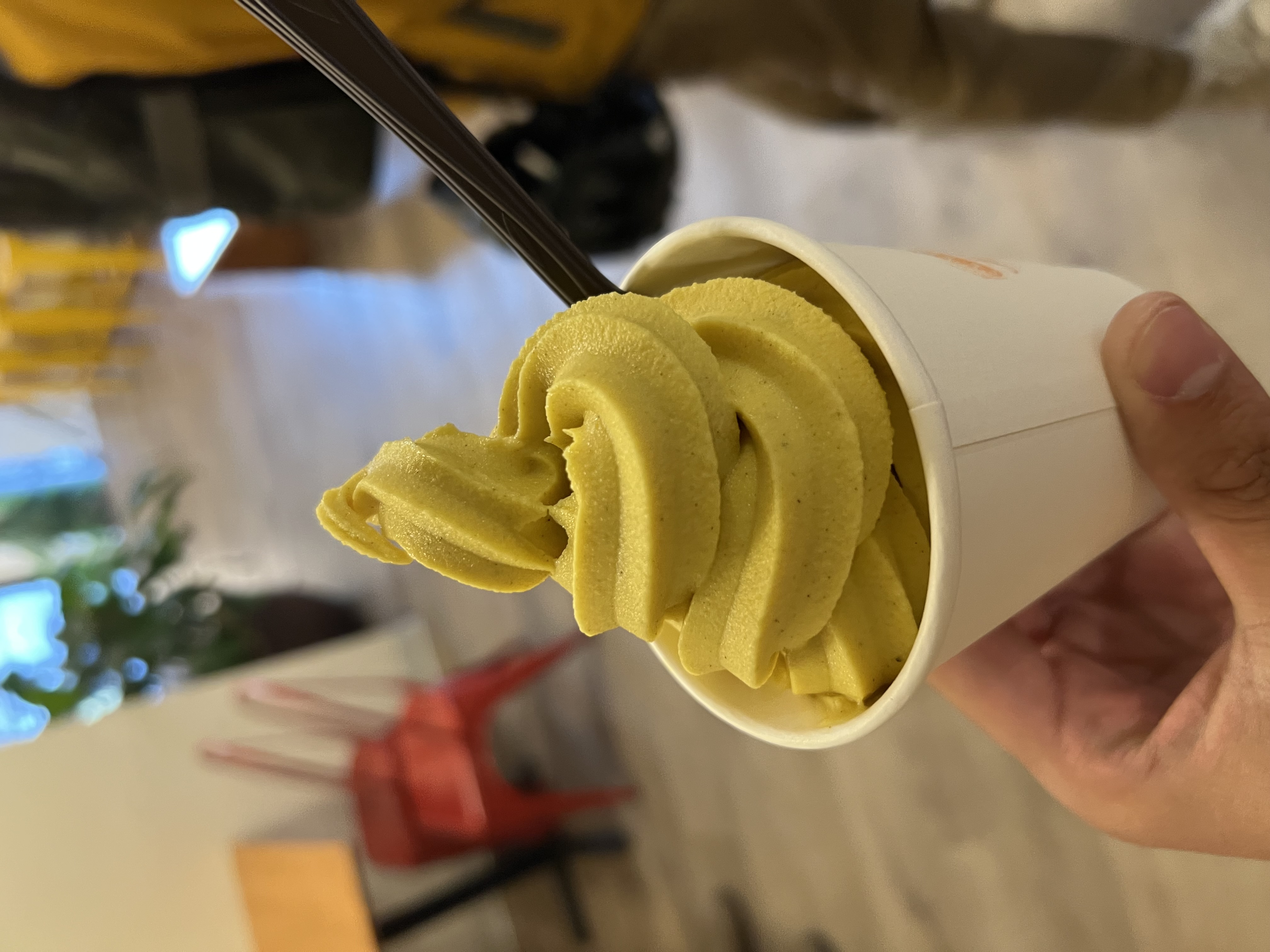 a cup of the Haldi Doodh soft serve with a spoon sticking out of it. The swirl of ice cream is bright yellow with flecks of spices mixed in.